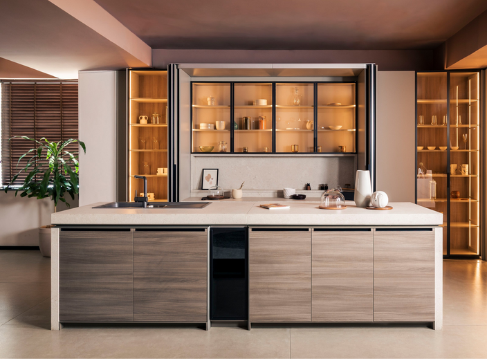 A modern kitchen island with light wood grain cabinets and a white countertop, set within a contemporary kitchen featuring warm ambient lighting, glass-front cabinets, and built-in appliances.3