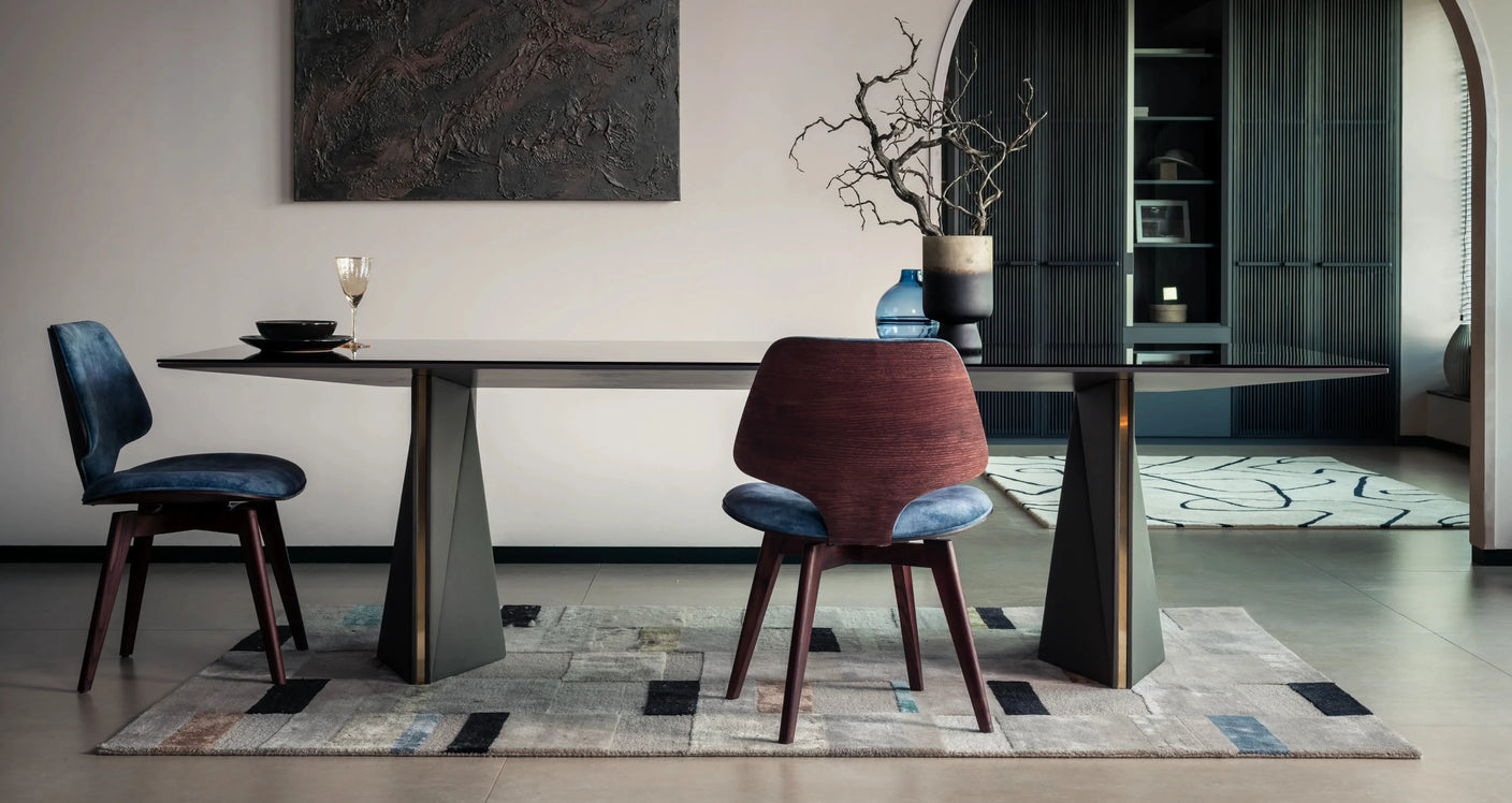 Modern dining room with a long table and chairs on a patterned rug.